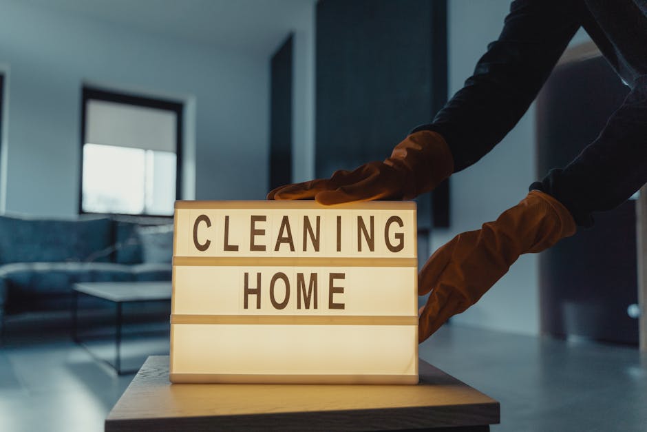 Three professional cleaners from Cleaners Shepherds Bush are positioned in a modern living room, performing surface cleaning and deep cleaning tasks. The room features a tiled floor, a dark-colored se
